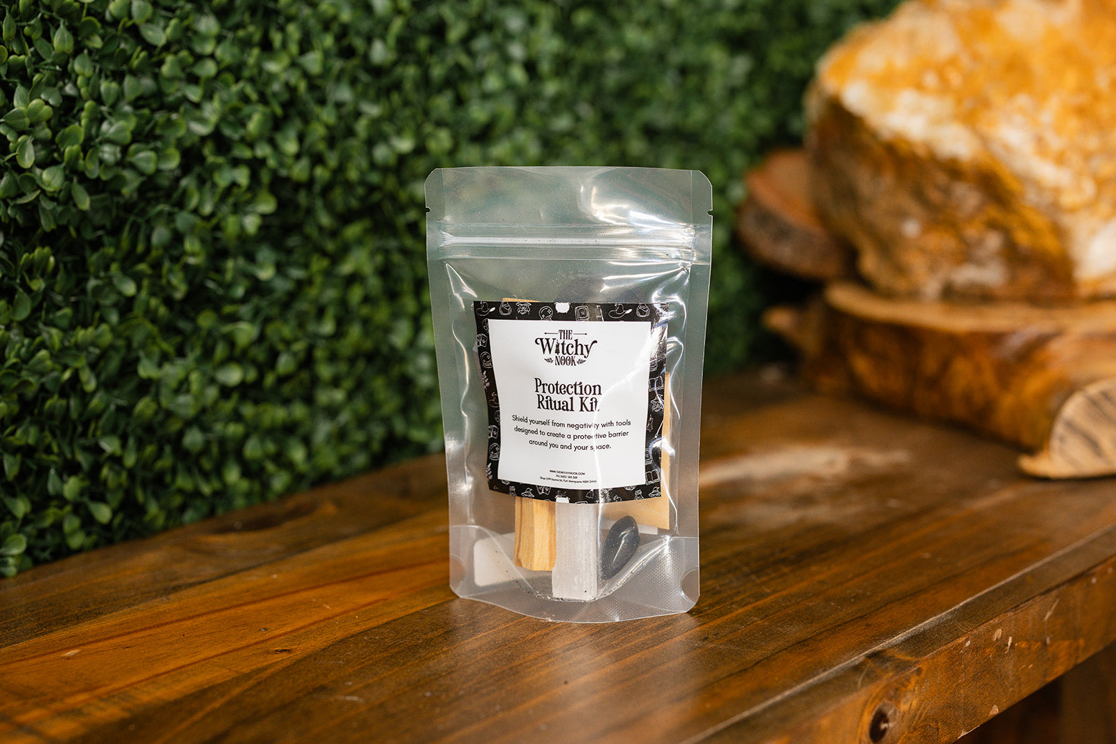 Packaged product labeled 'Protection Ritual Kit' by 'Witchy Nook' on a wooden surface with greenery in the background.