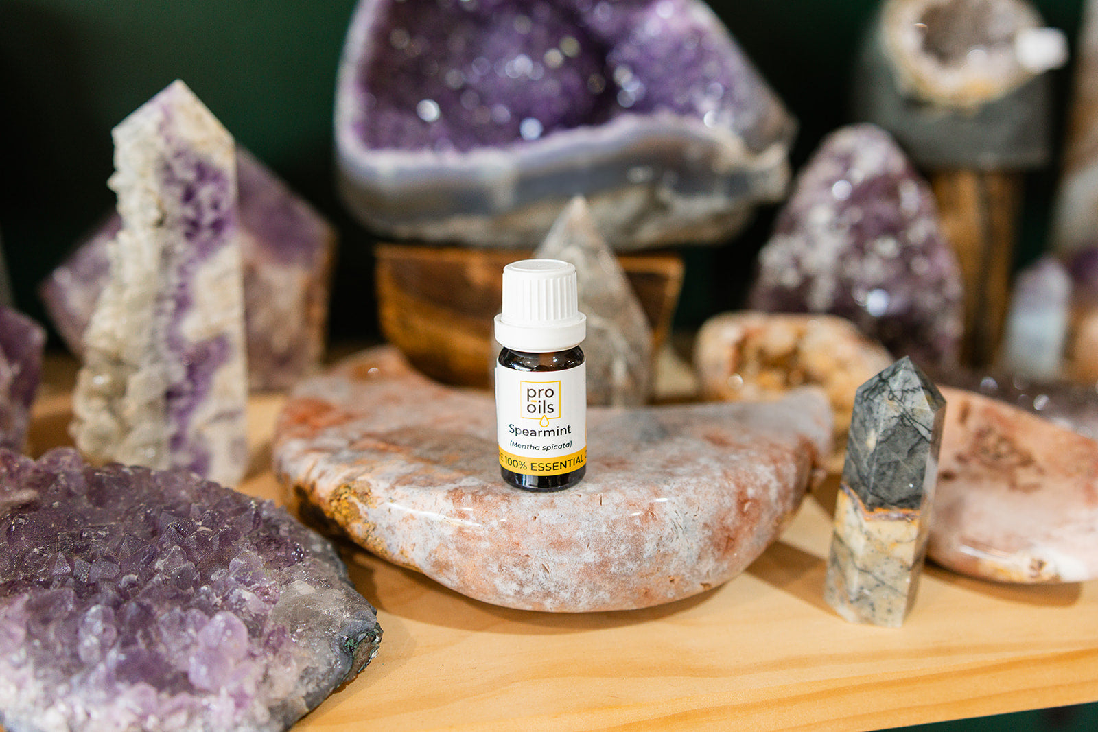 Small bottle of Spearmint Essential Oil on a wooden surface with crystals in the background