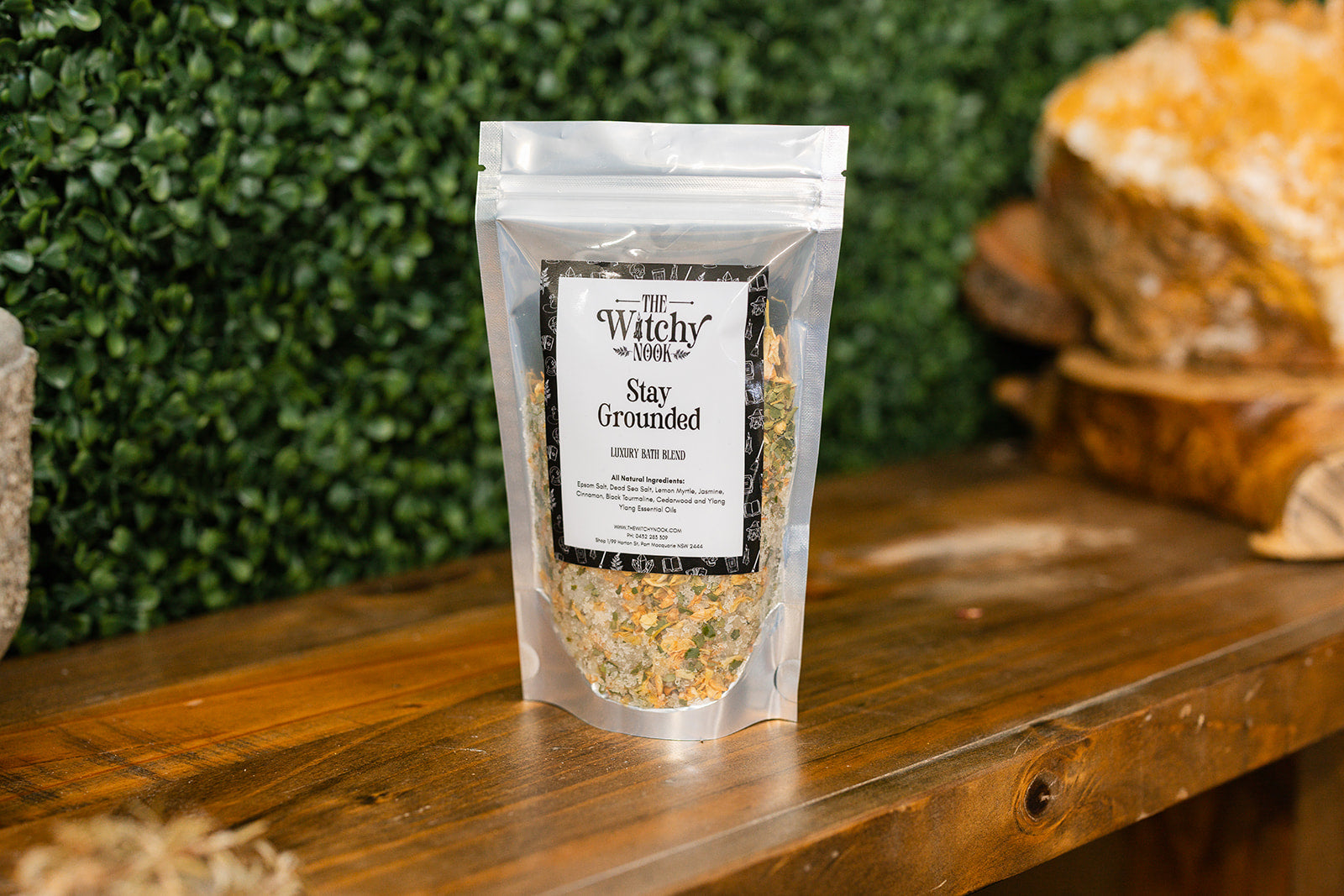 Packaged product labeled 'Stay Grounded' by 'Witchy Nook' on a wooden surface with greenery in the background.