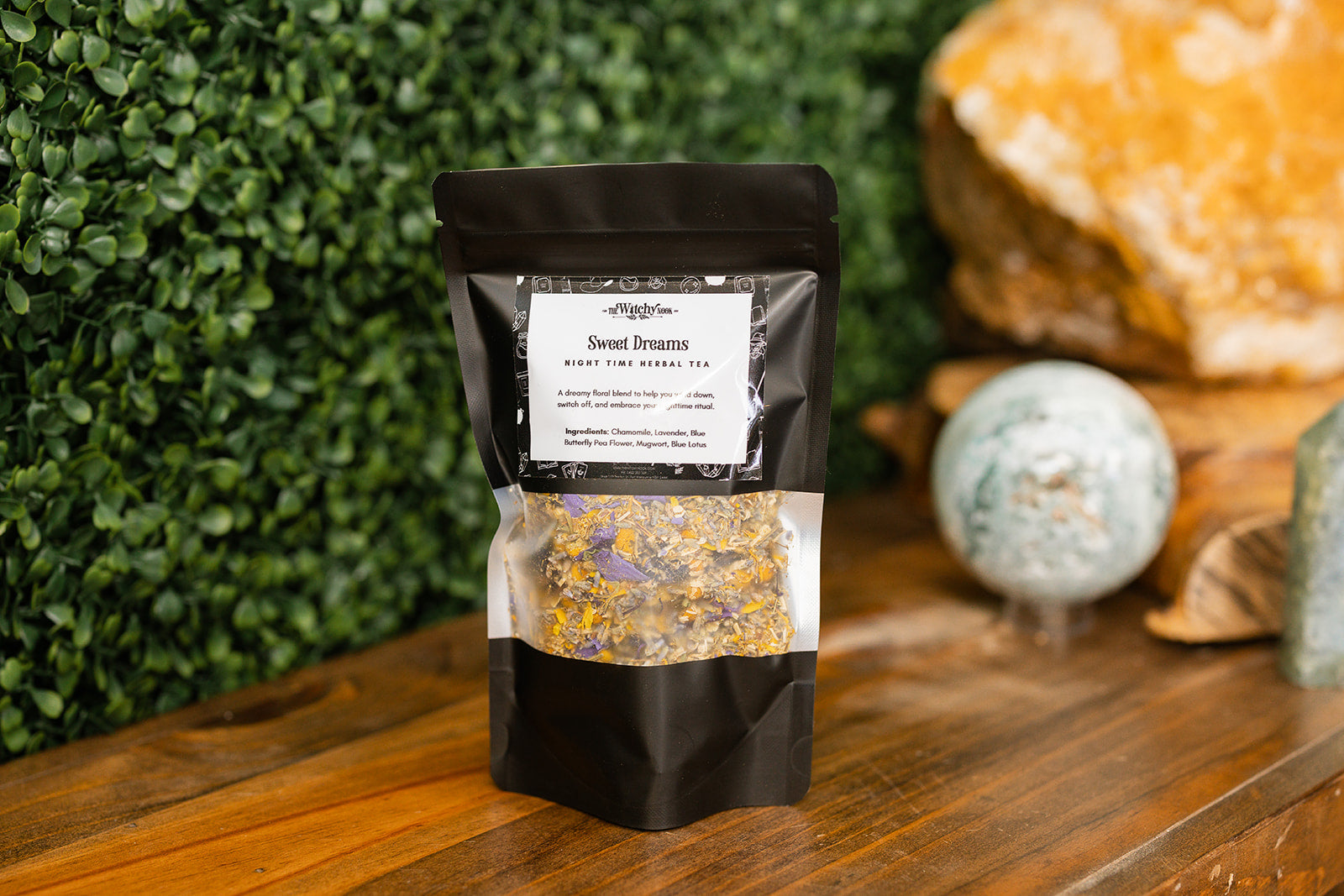 Black tea packaging with visible product on a wooden surface with greenery in the background