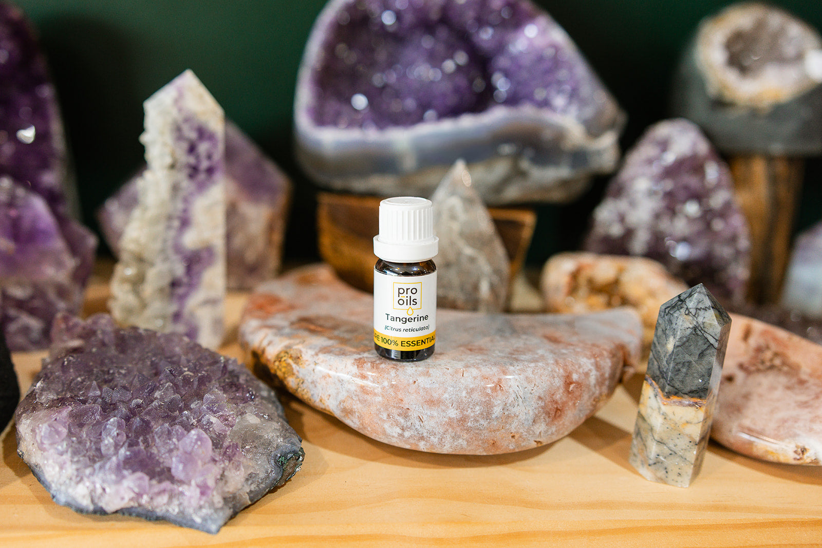 Small bottle of essential oils surrounded by amethyst crystals on a wooden surface