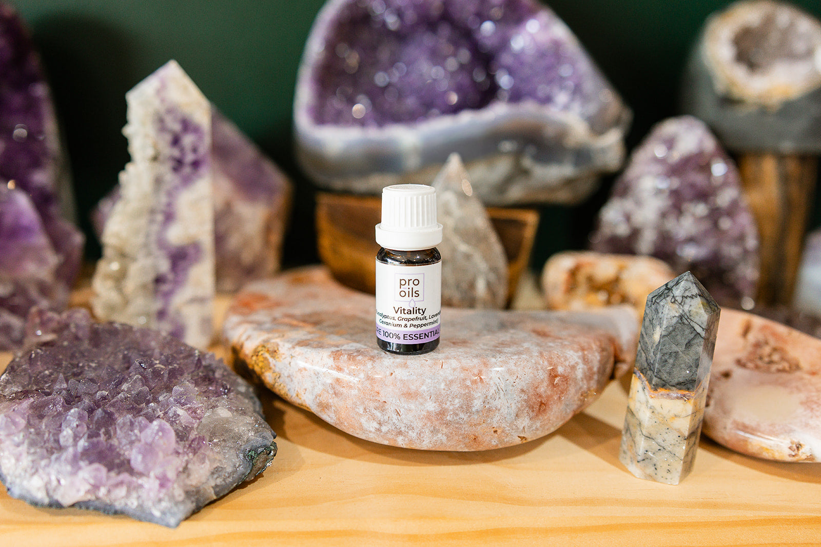 Small bottle of Vitality Essential Oil Blend oil on a wooden surface with crystals in the background