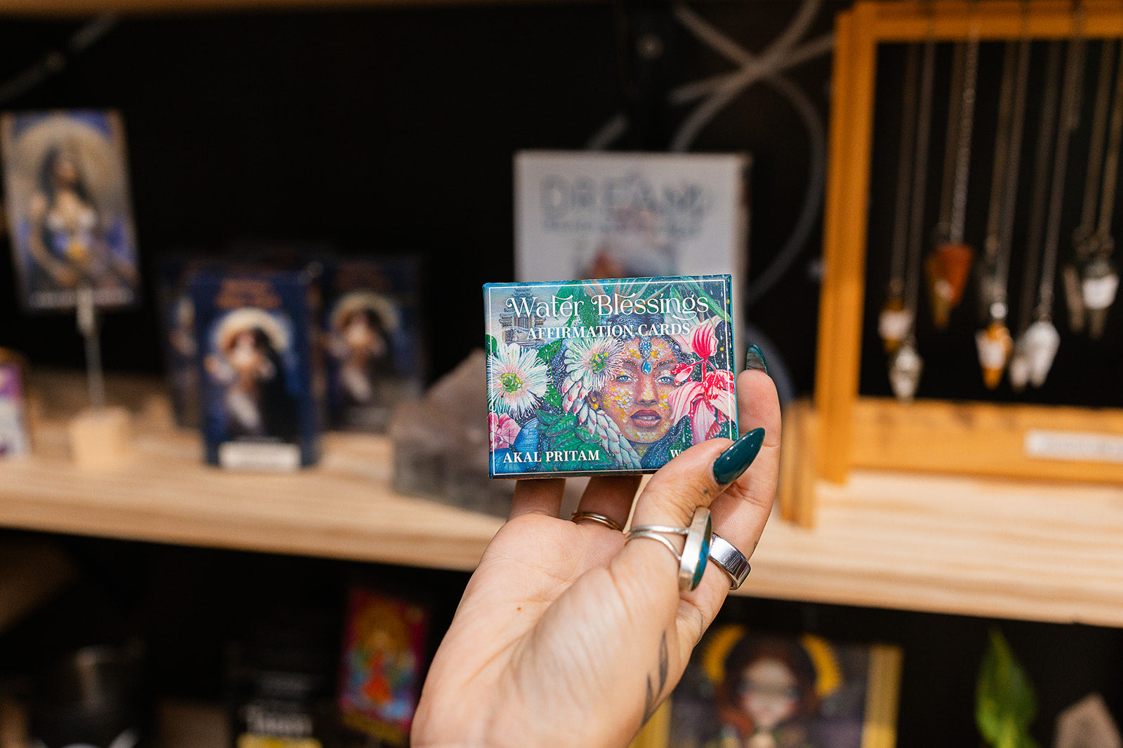 Hand holding a deck of cards with a colorful design, surrounded by shelves with more cards and jewelry.