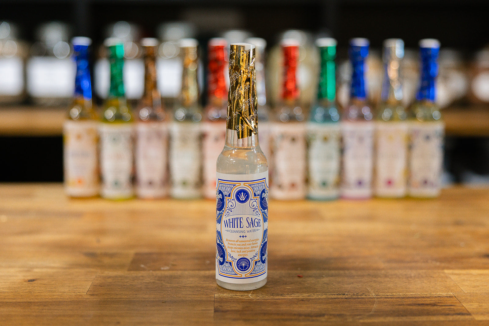 Bottle of White Sage cleansing water on a wooden surface with blurred bottles in the background