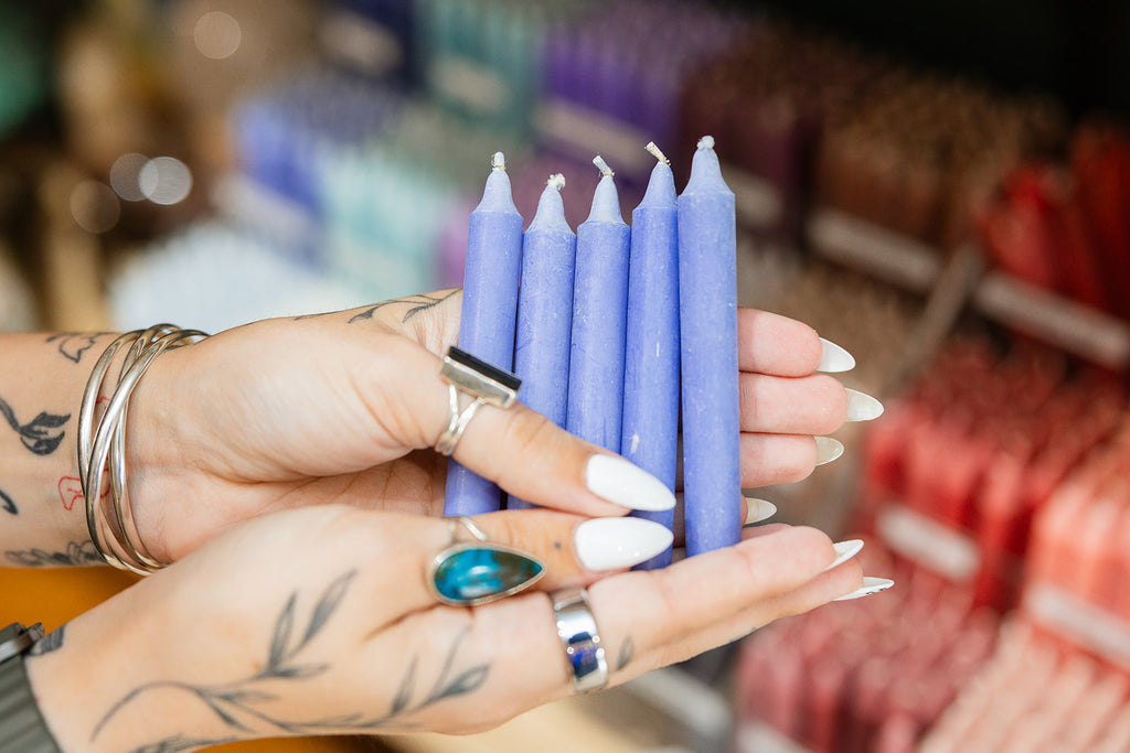 Hands holding blue candles with a blurred background of more candles.