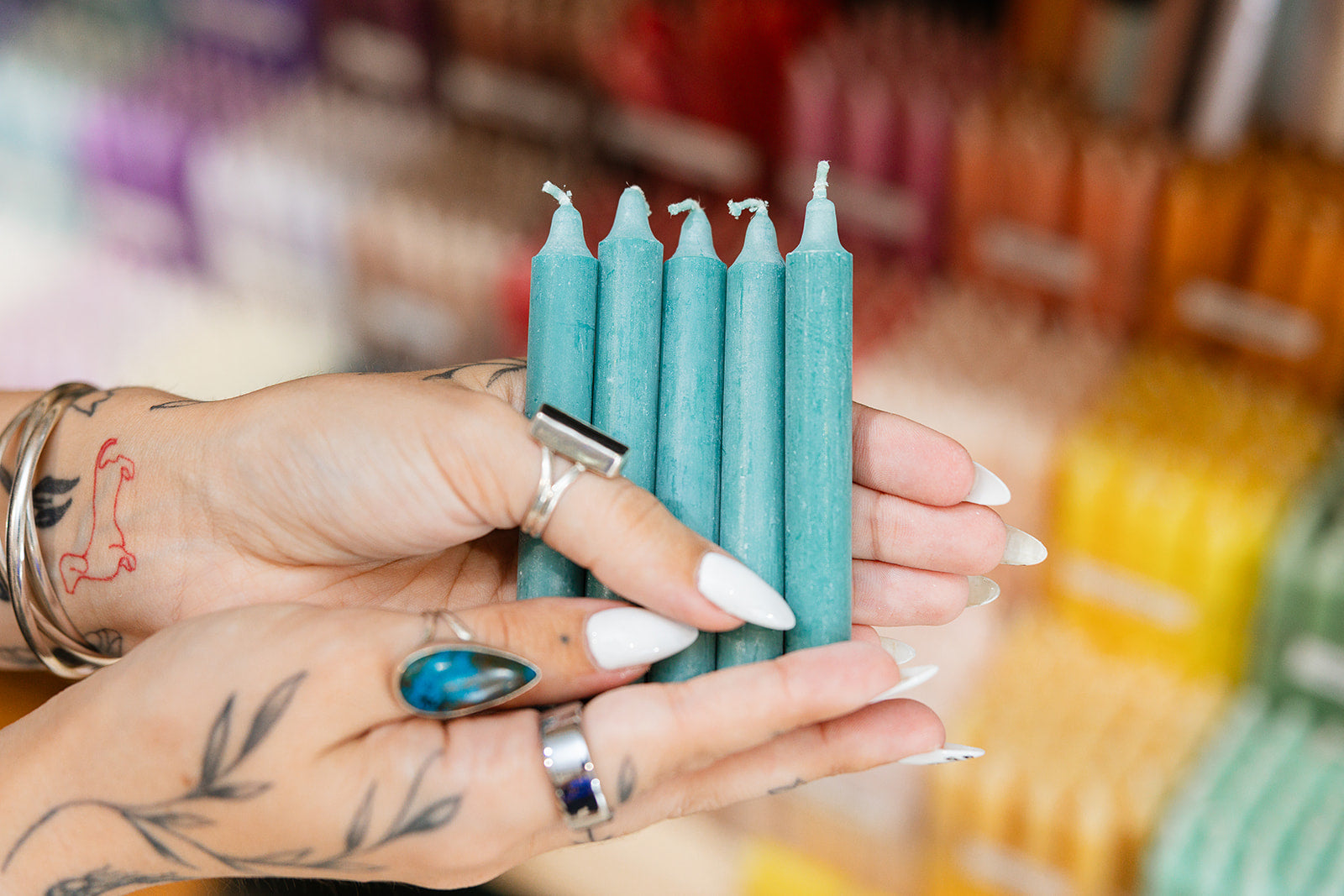 Hand holding teal candles with a blurred candle store background