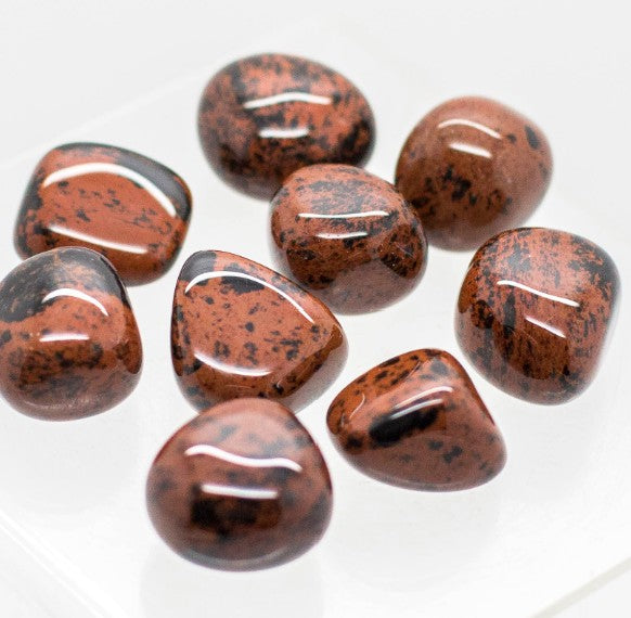 The image displays a collection of polished Mahogany Obsidian tumbled stones on arranged on a white background