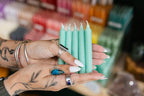 Person holding mint green candles with a blurred candle display in the background