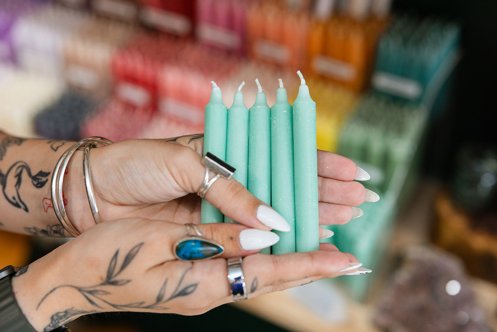 Person holding mint green candles with a blurred candle display in the background