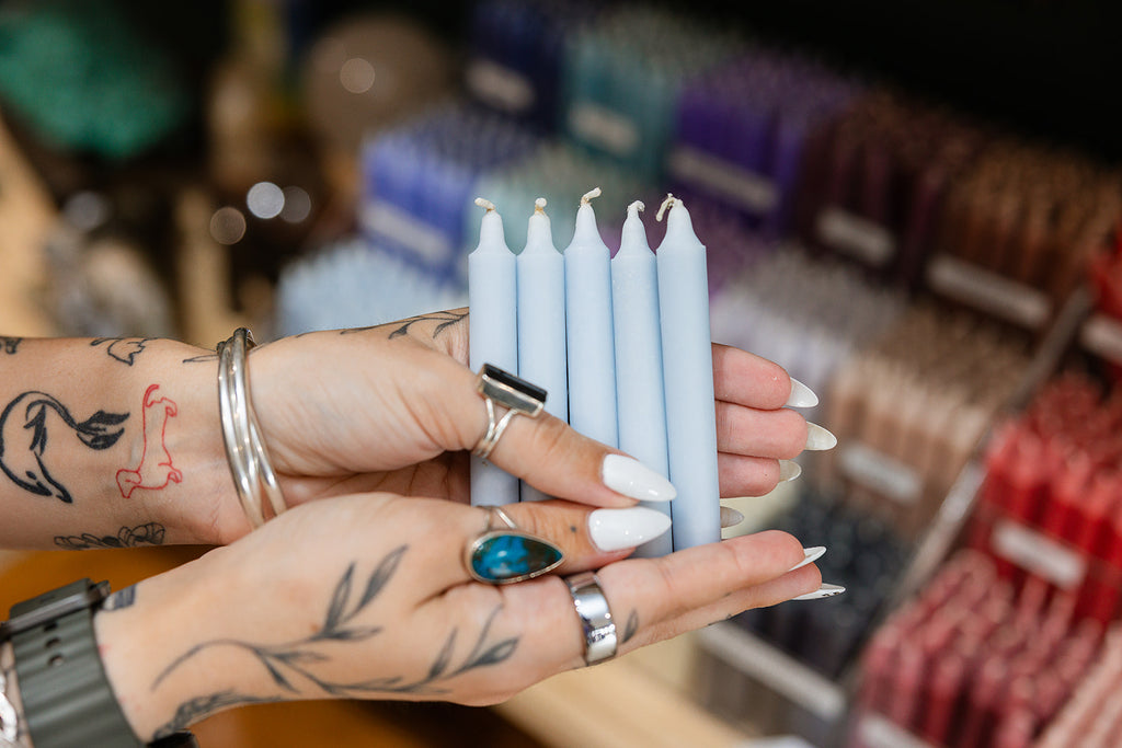 Hands holding light blue candles with a blurred background of colorful candles