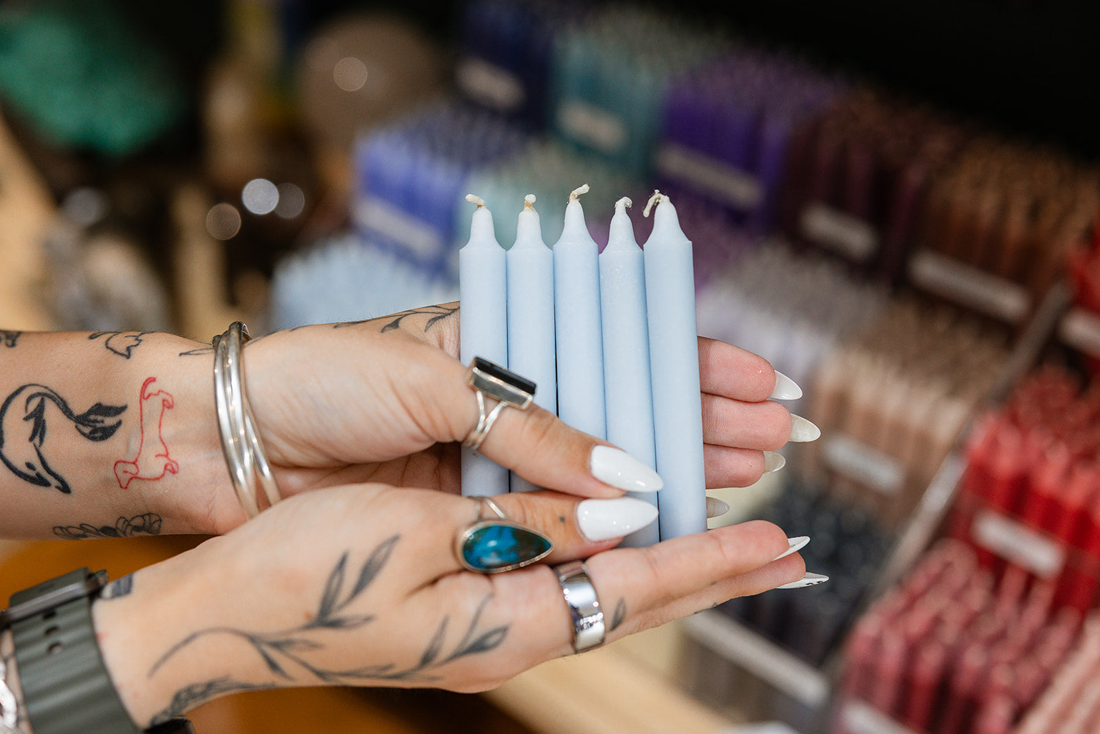 Hands holding light blue candles with a blurred background of colorful candles
