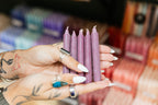 Hand holding plum purple candles with a blurred background of colorful items