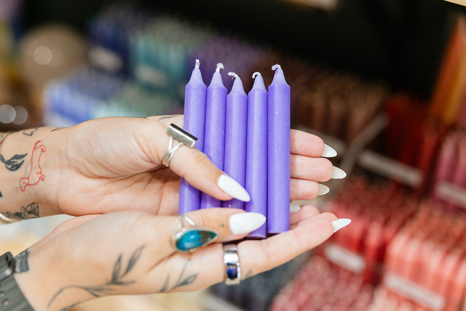Purple candles held by a person with tattoos and nail polish.