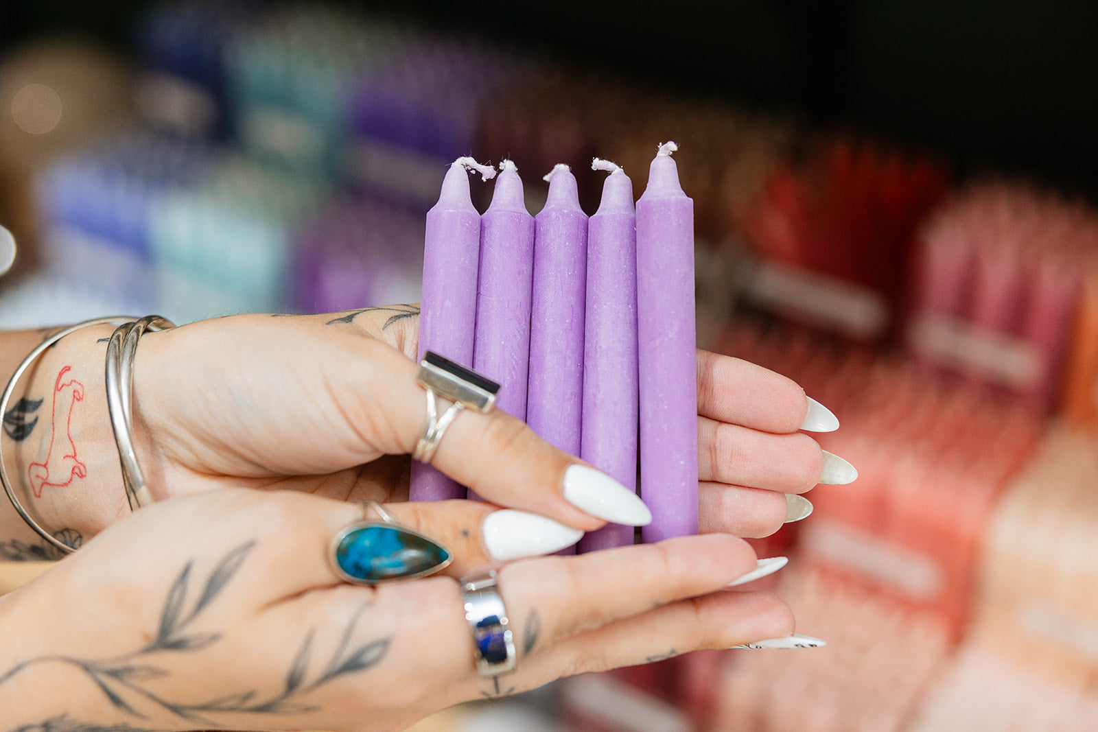 Purple candles held by a person with tattoos and rings in a blurred store setting