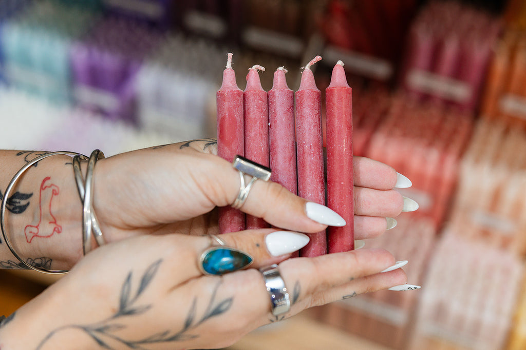 Person holding red candles with tattoos and rings visible