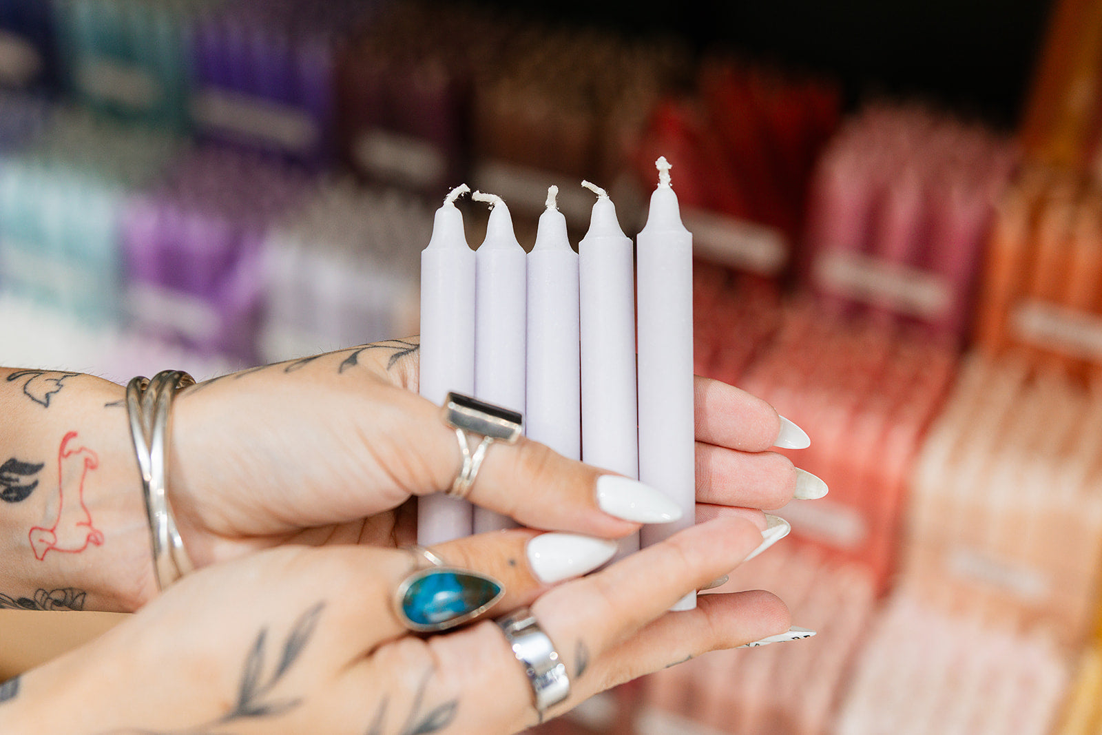 Person holding silver candles with a blurred background of colorful items