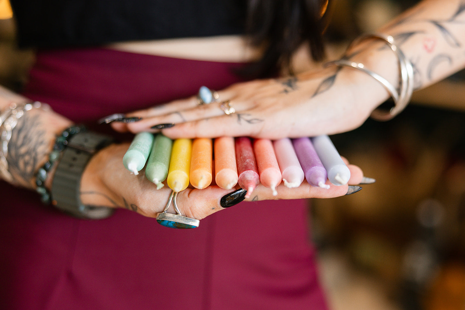 Colorful candles held by a person with tattoos, with a blurred background