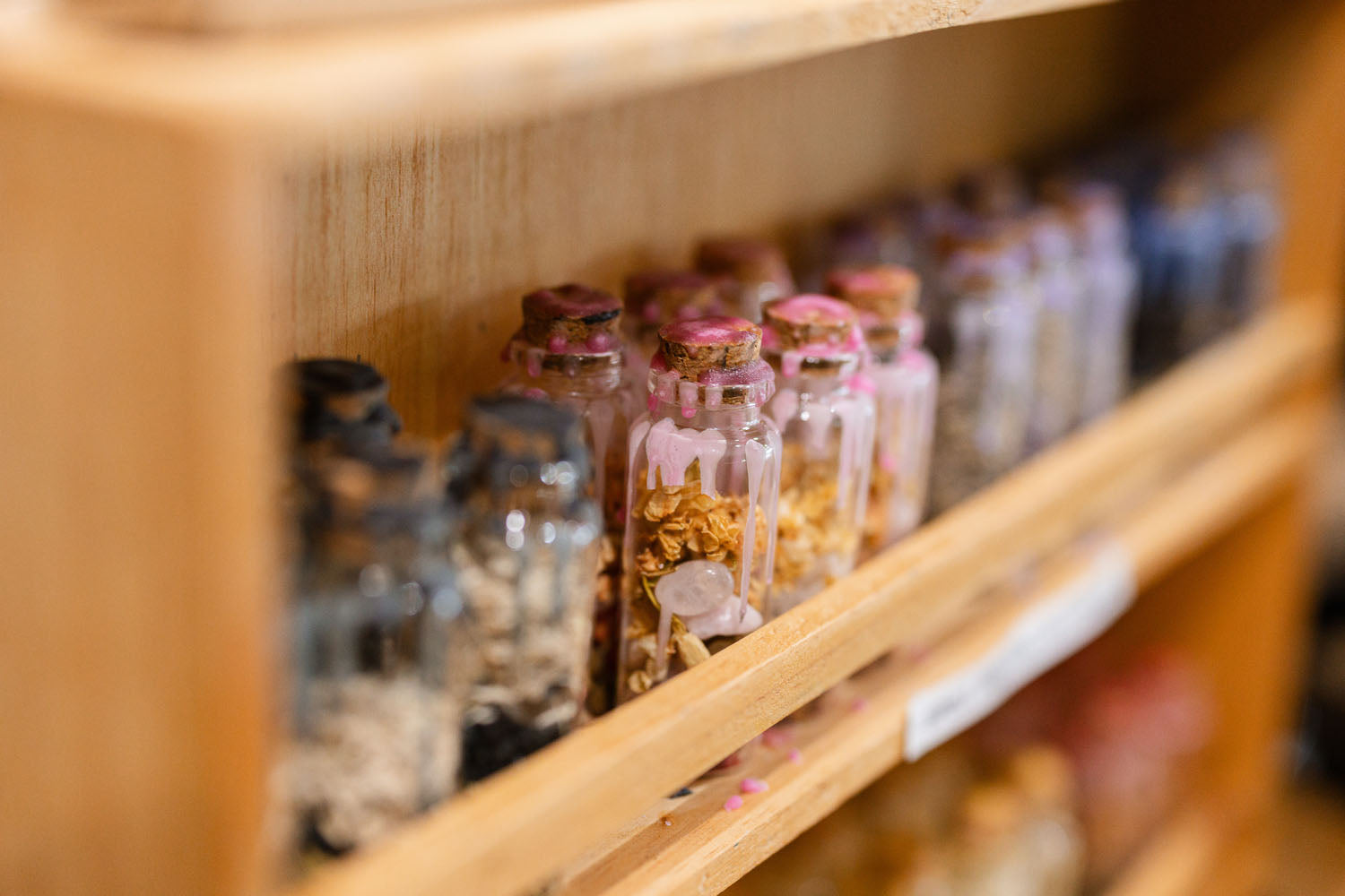 Row of small glass spell jars with various contents on a wooden shelf.