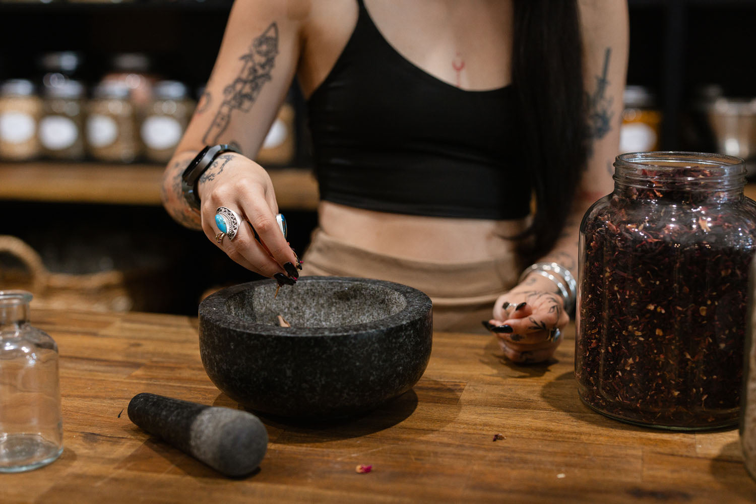 Person using a mortar and pestle on a wooden table with jars in the background