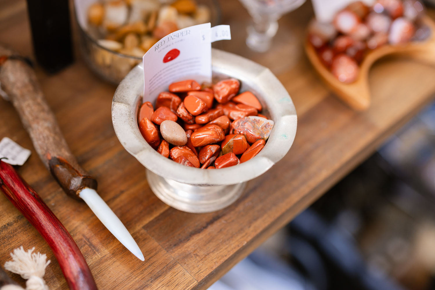 Small metal vessel filled with red stones on a wooden surface with tools and blurred background