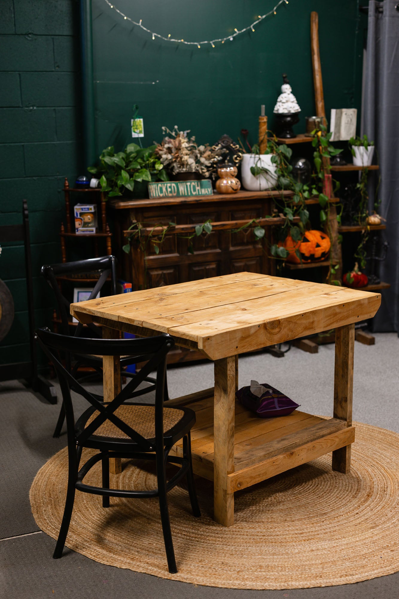 Wooden table with a black chair on a round rug against a green wall with decorative elements.