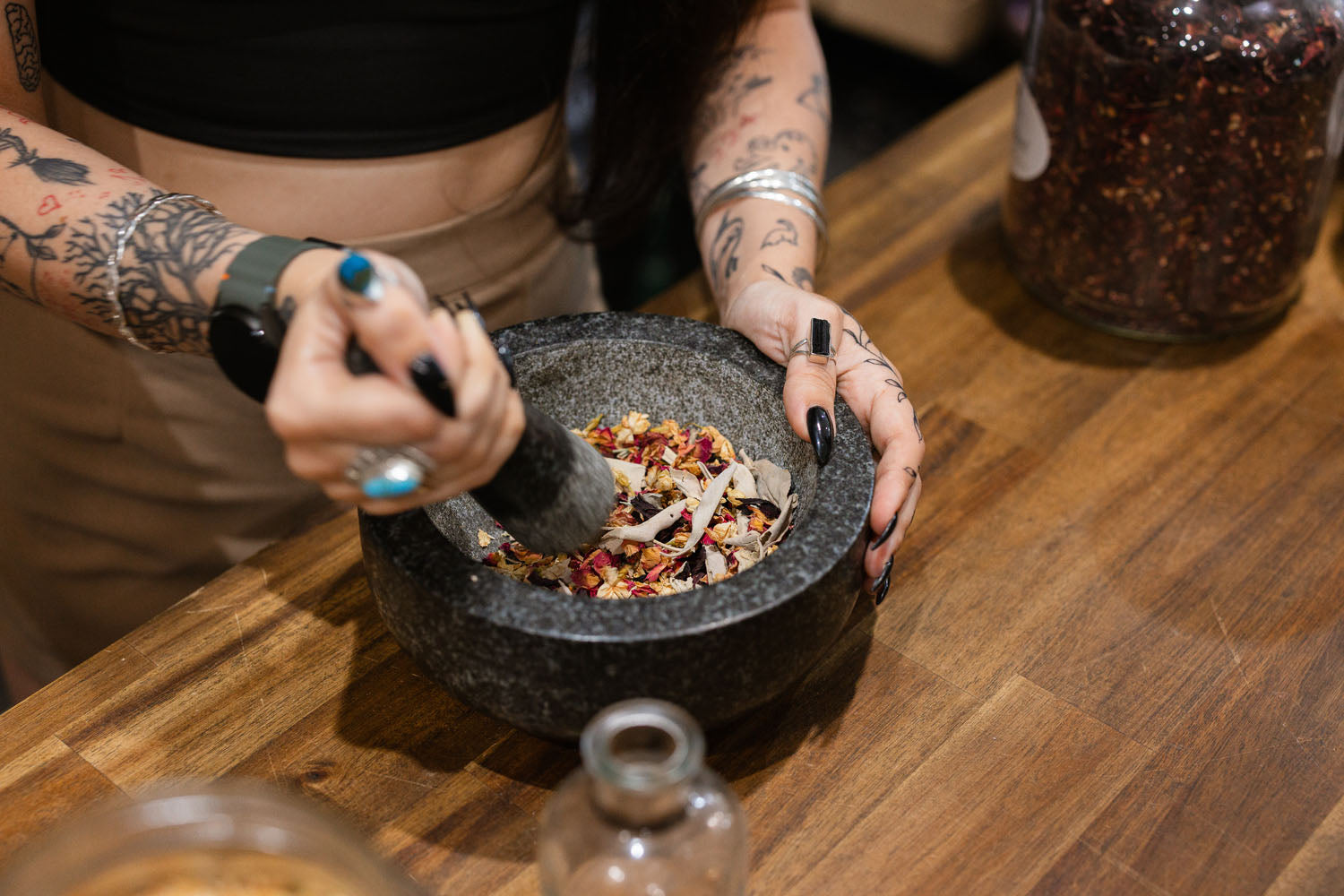 Person using a mortar and pestle crushing herbs on a wooden surface
